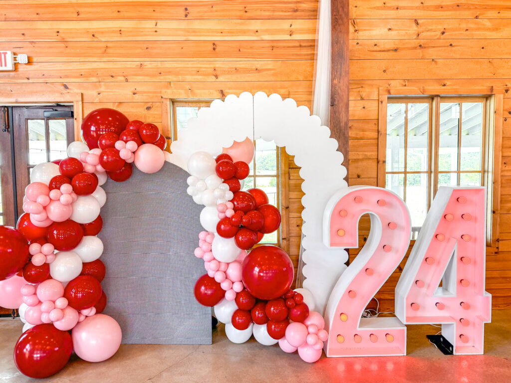 Another smaller balloon arch, along with tall light-up "'24" signs with an additional white archway in the middle.