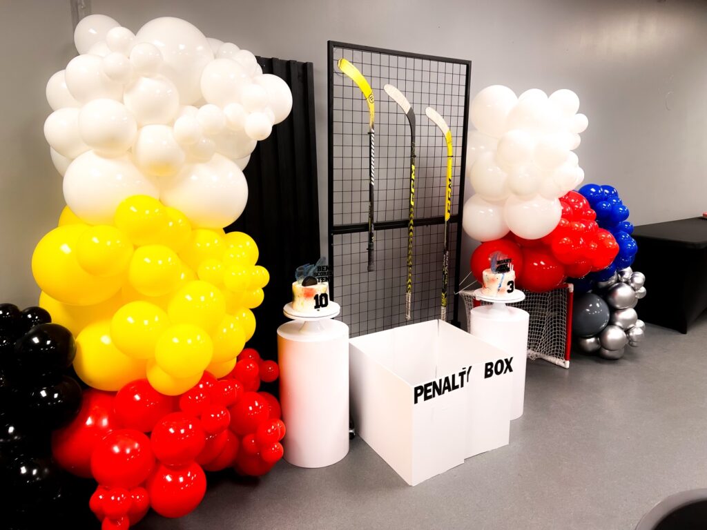 Hockey birthday party set up. Has hockey sticks, balloon arches, and cute little penalty box in front of the cakes