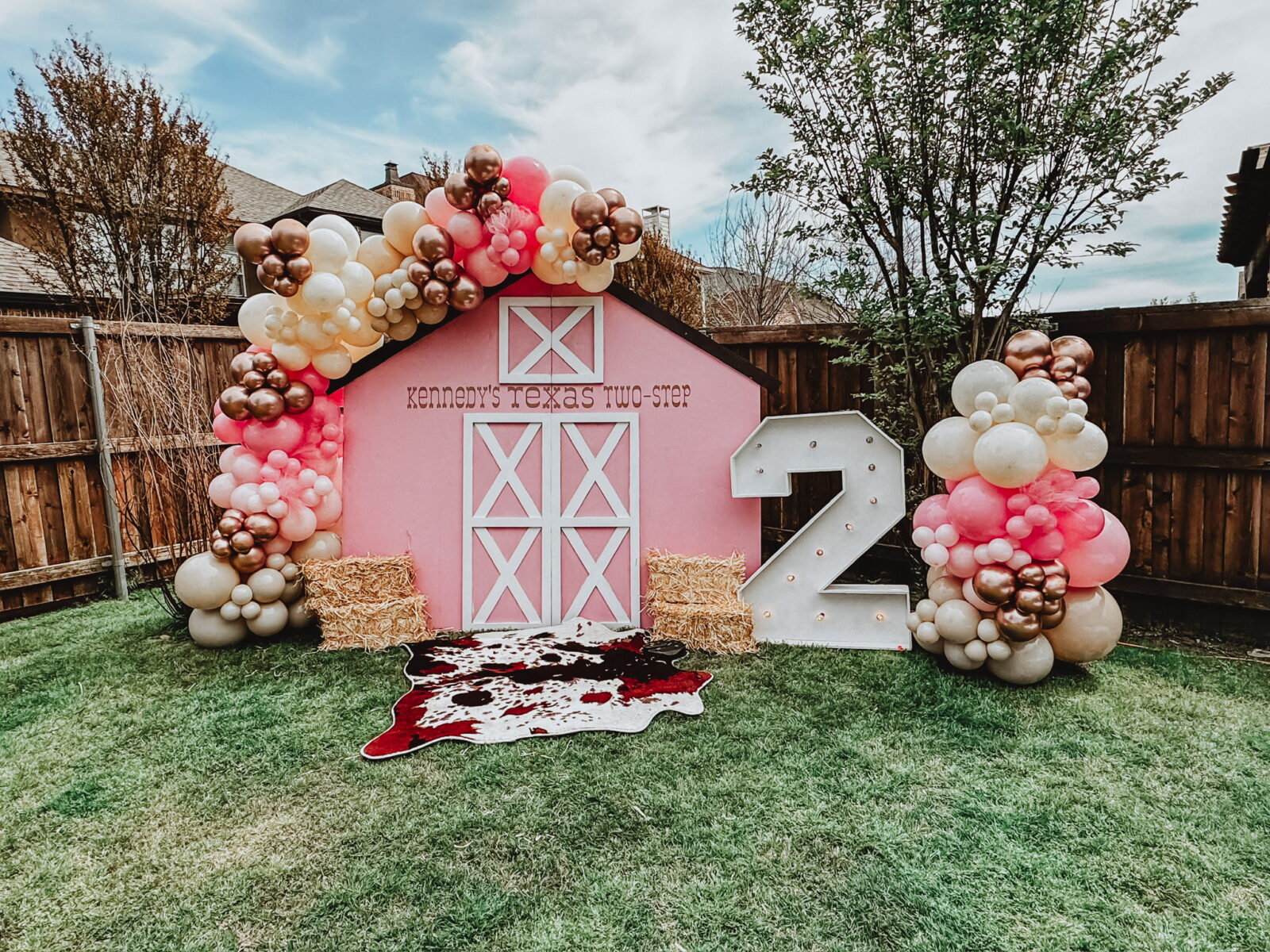 Girl's birthday party with pink barn door backdrop and balloon arched. Cowhide, big light up #2, and hay bails are sitting in front.