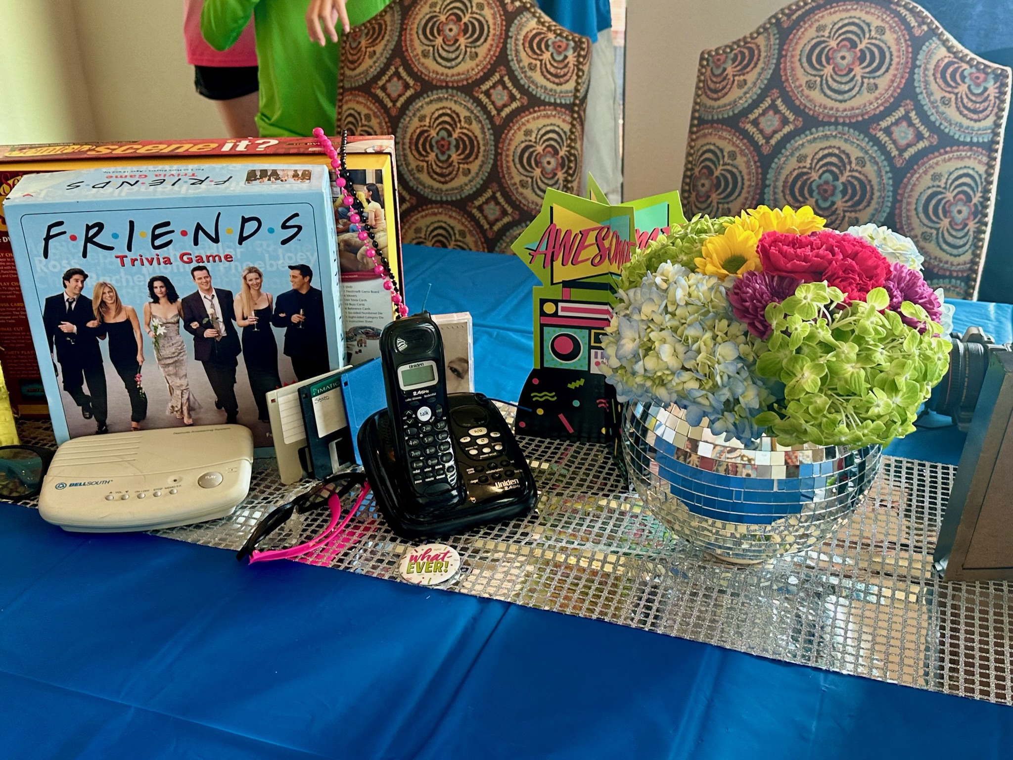 Table with boardgames and old landline phone with a disco ball vase with flowers.