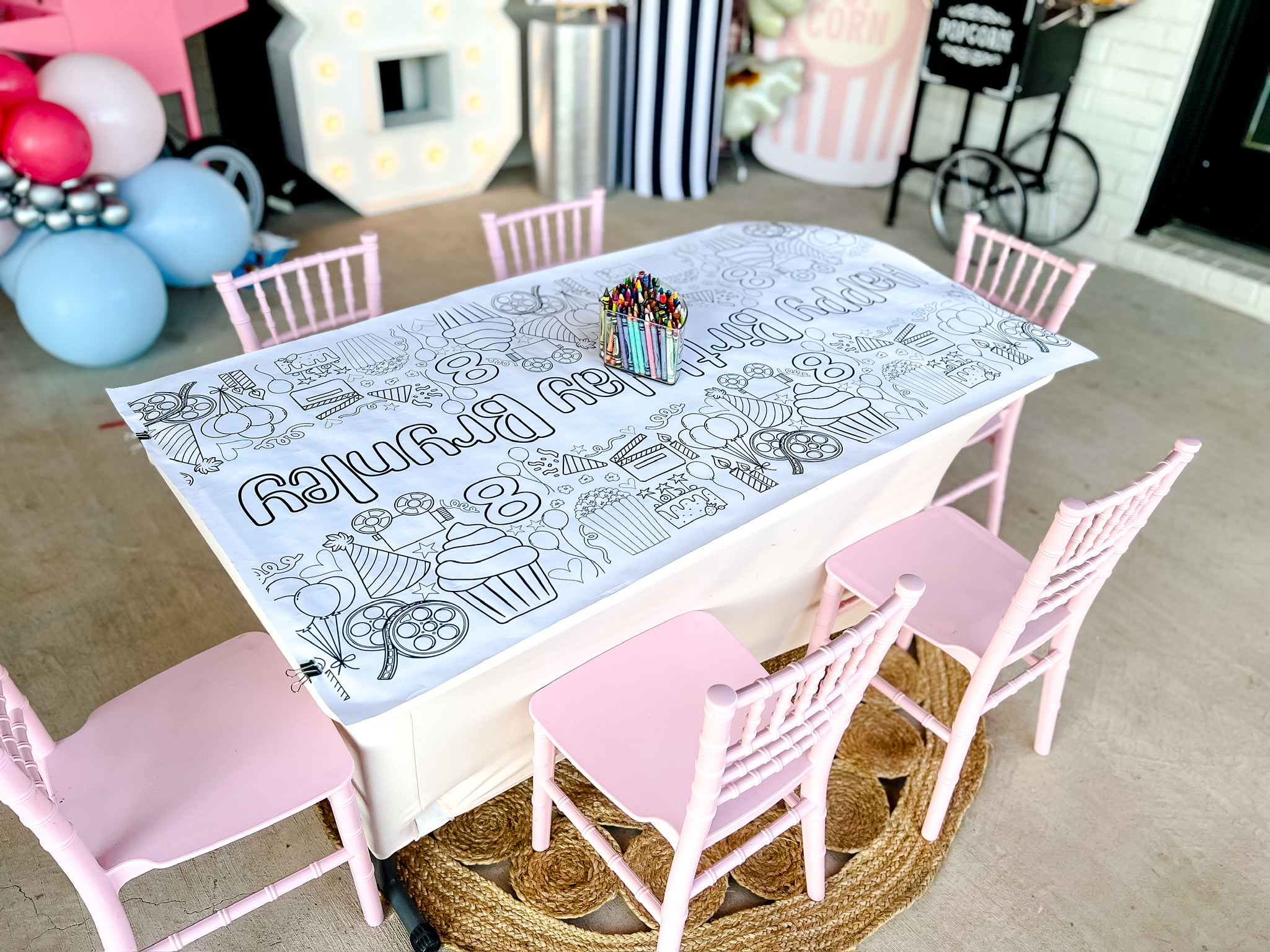 table with crayons and coloring mat, white spandex table cover, light pink chairs, woven round rug