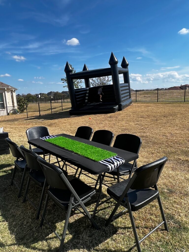 football birthday bash set up, black bounce house, black table with chairs, black and white striped table runner, turf table runner, backyard football birthday set up