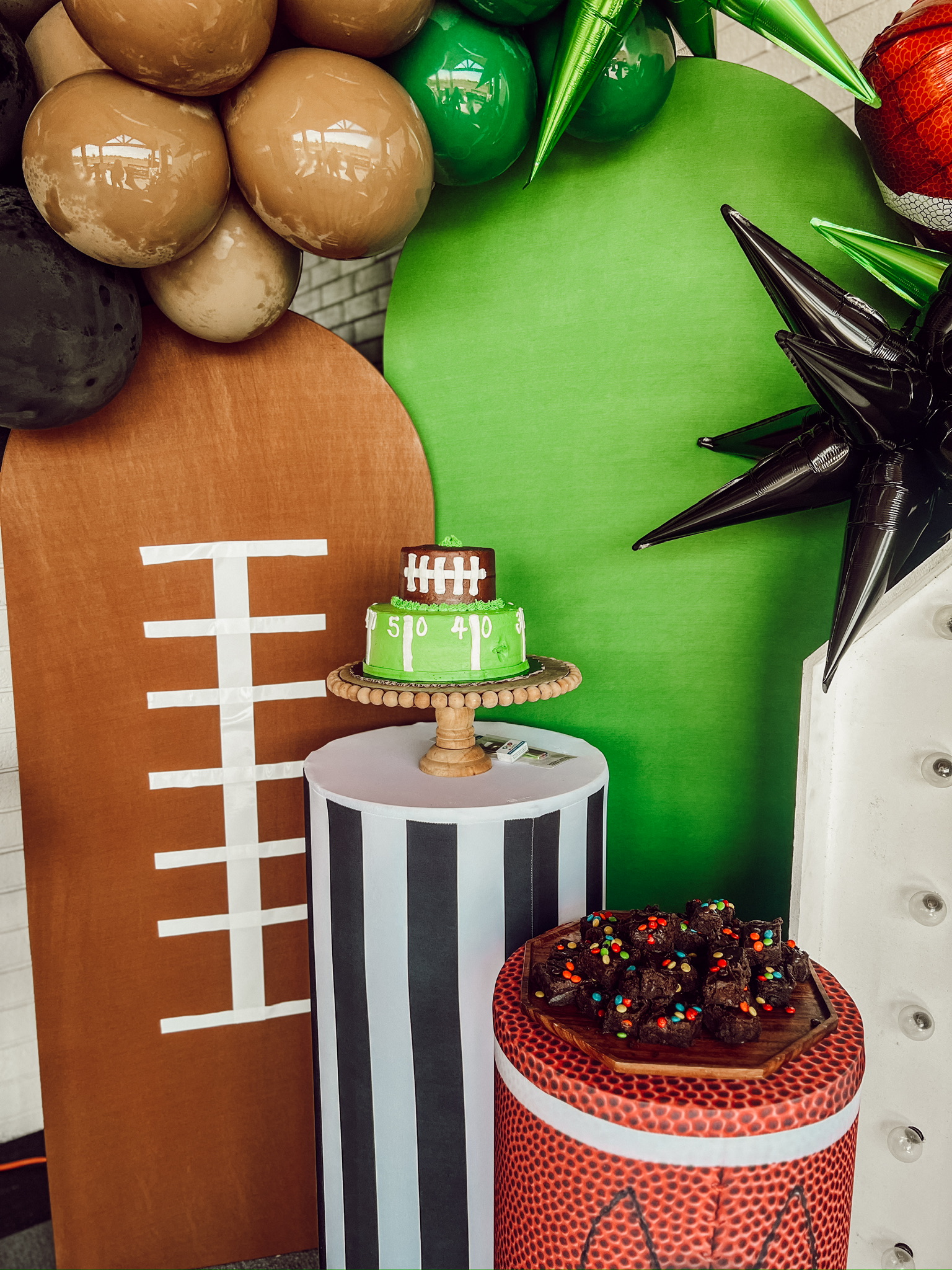 football birthday bash set up, arched wood backdrops, sports-themed backdrops, green and black star balloons, football-themed cake, brownies, sports-themed cylinder plinth covers